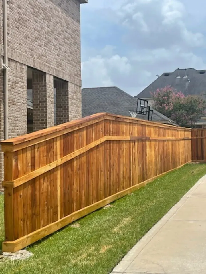 Cedar fence with cap and trim and a stepped top rail beside a brick home