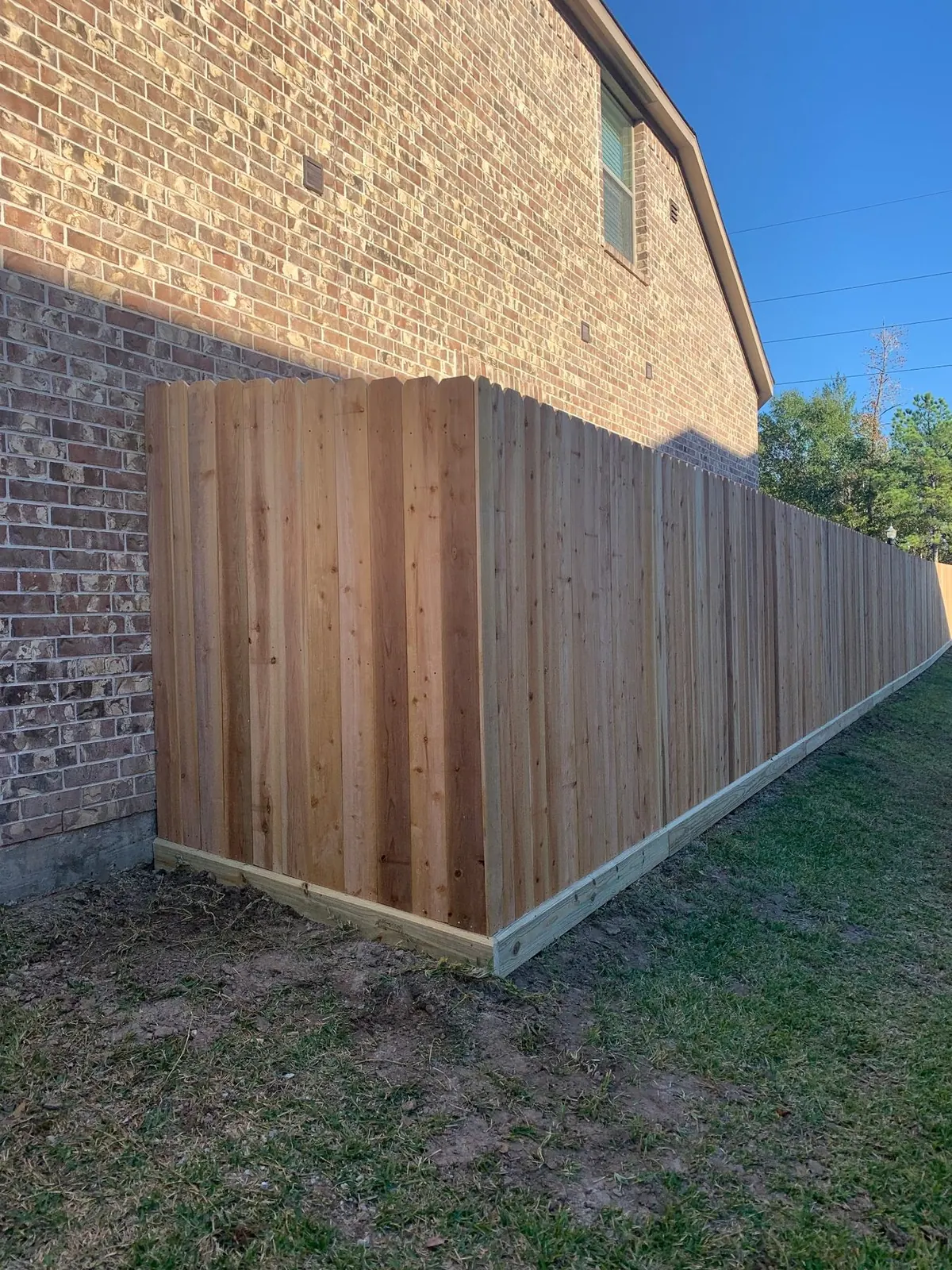 Finished cedar privacy fence beside a two-story brick home