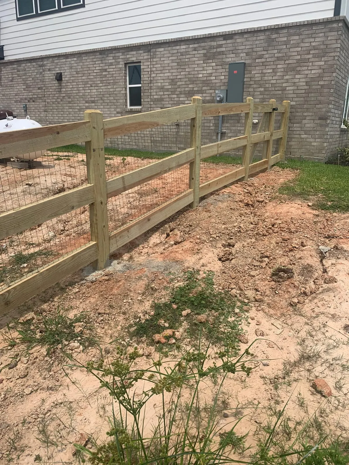 Wood ranch-style rail fence going up beside a Katy home