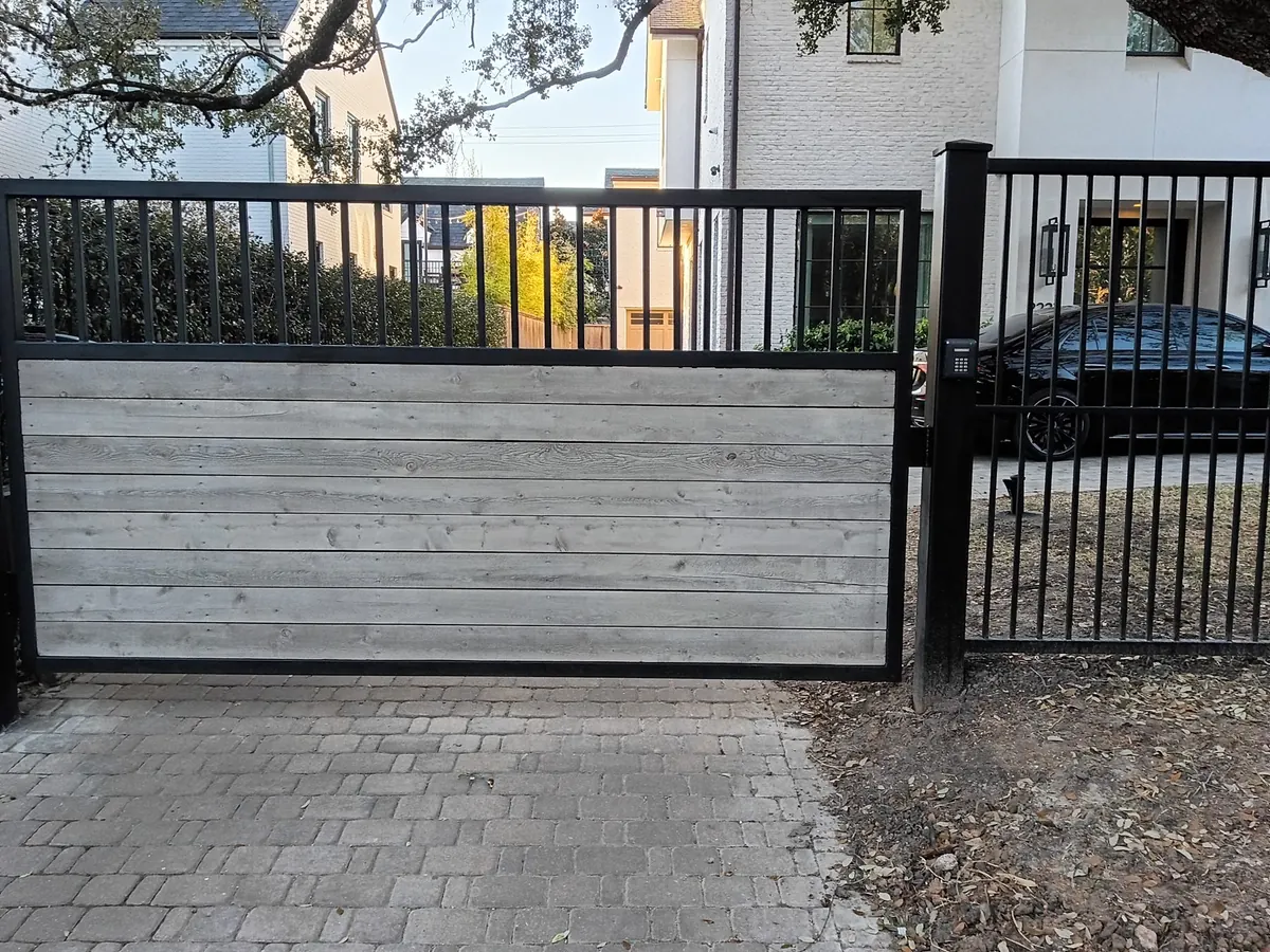 Sliding driveway gate with a metal picket panel in front of a modern home