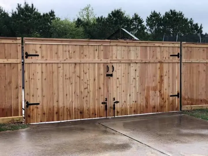Large swinging double wood driveway gate with black hardware in Katy