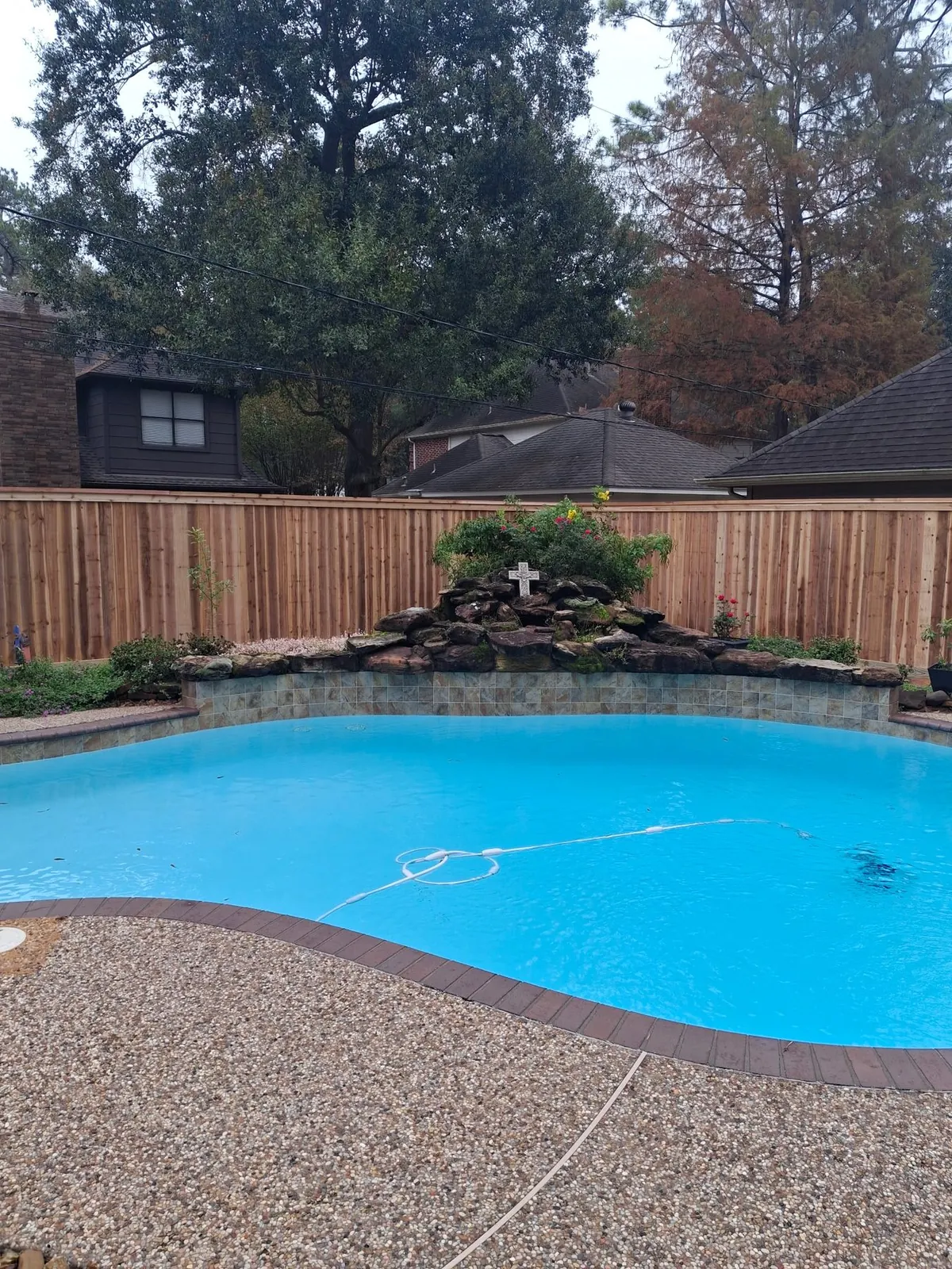 Cedar privacy fence behind a backyard pool and rock waterfall in Fulshear