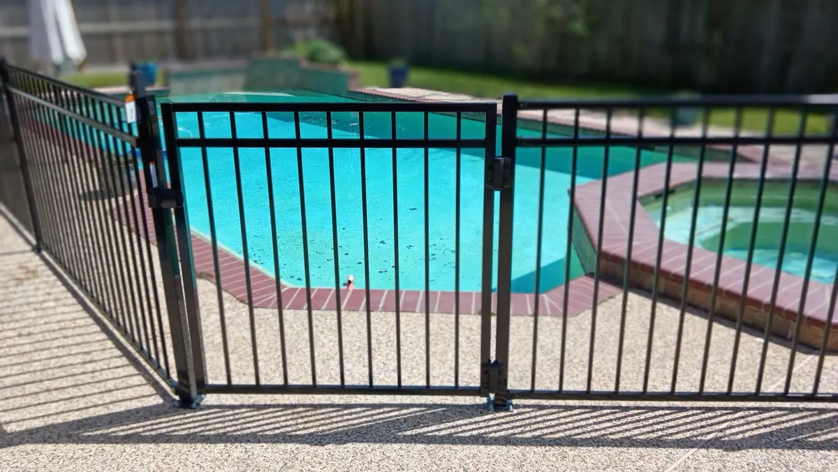 Black metal pool fence and gate around a backyard pool in Katy