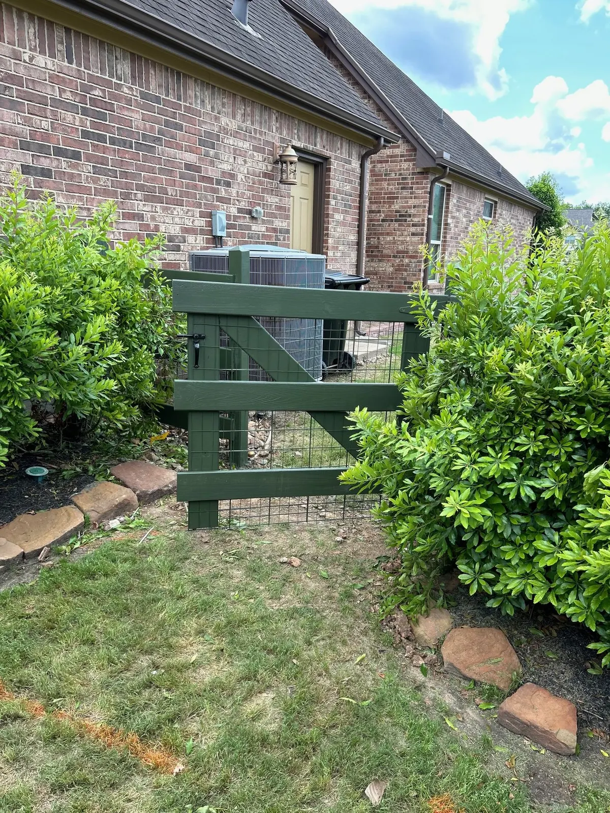 Green-painted split rail fence and gate beside a brick home in Fulshear